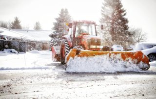 A snowplow clearing a snowy road with trees in the background.